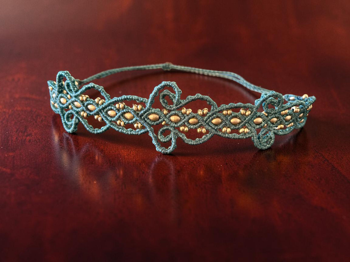 Teal and gold macramé lace choker on a dark wood surface