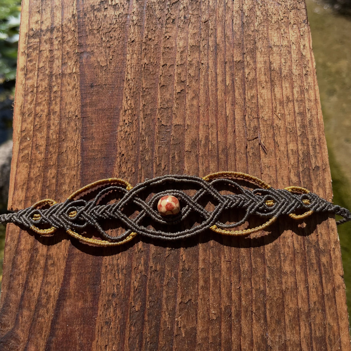 Dark macrame Celtic knot choker with stone bead displayed flat on natural wood