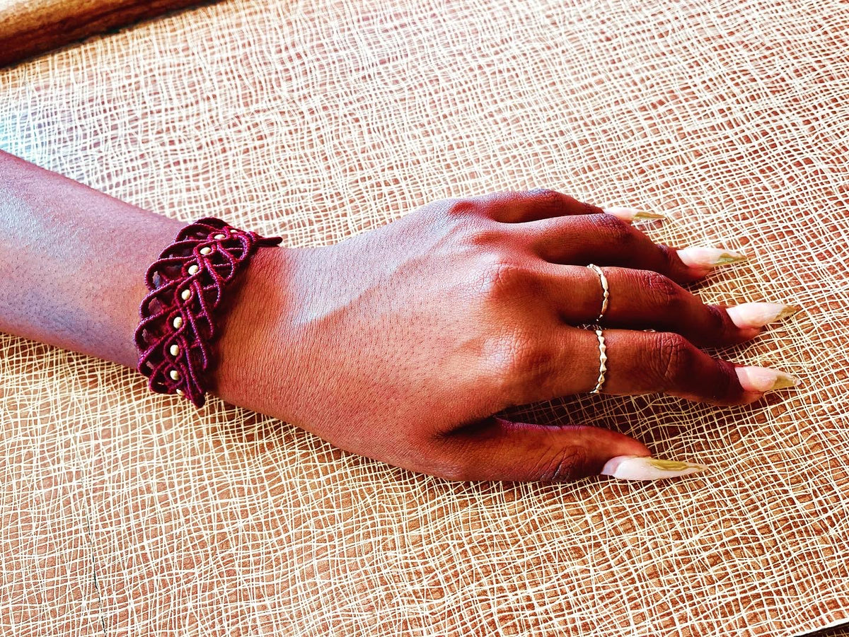 Burgundy macrame bracelet with gold bead accents worn on wrist
